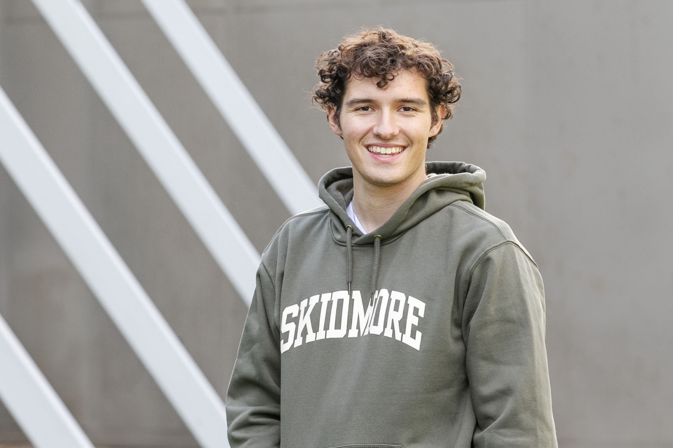 Braedon Quinlan ’24 smiles at the camera while wearing a ¼ϲʿ sweatshirt in front of the Tang Teaching Museum.