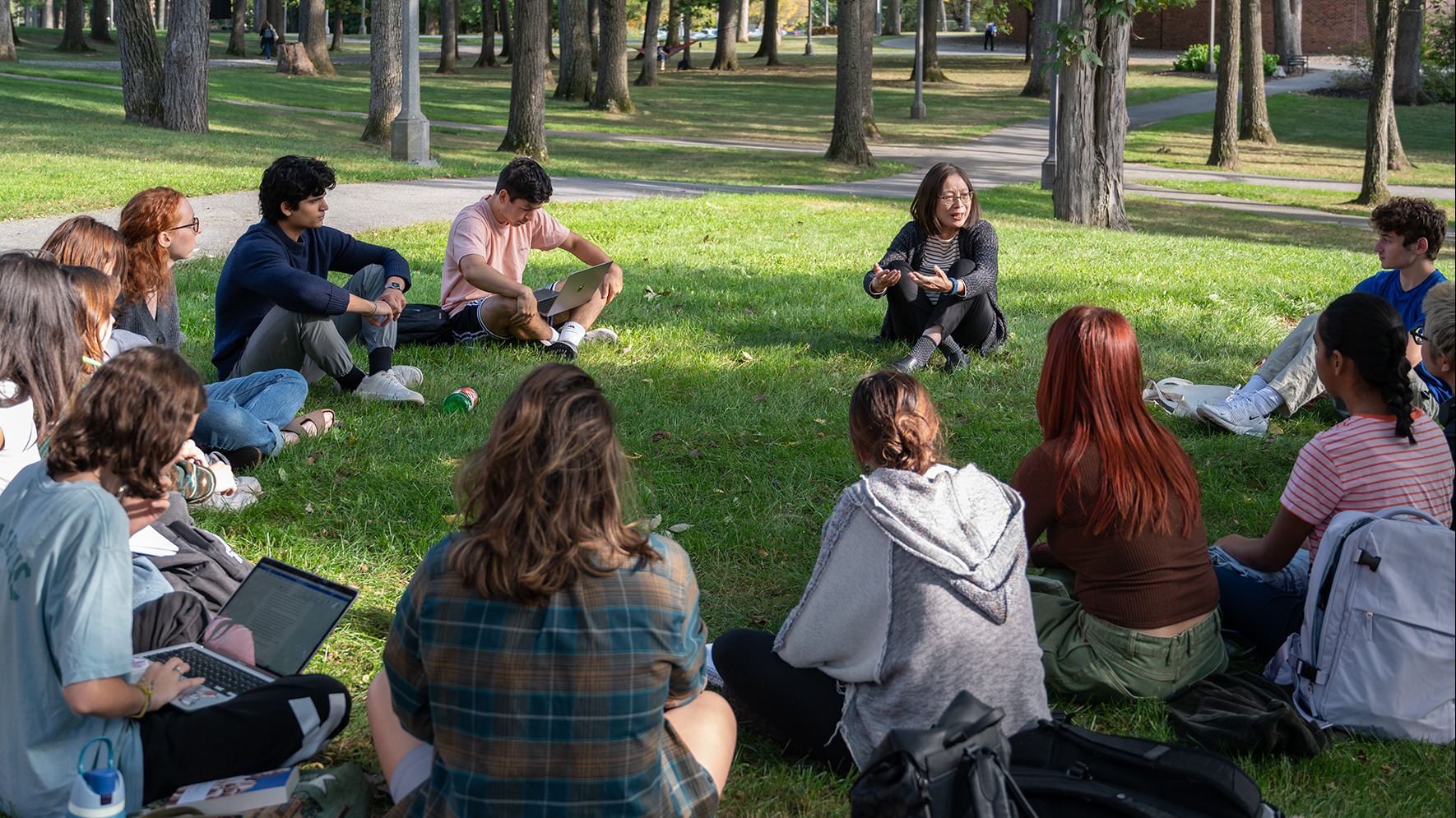Professor Mao Chen sits in a circle on the ¼ϲʿ green with her Ideal Worlds students. They listen, engaged, as she speaks.
